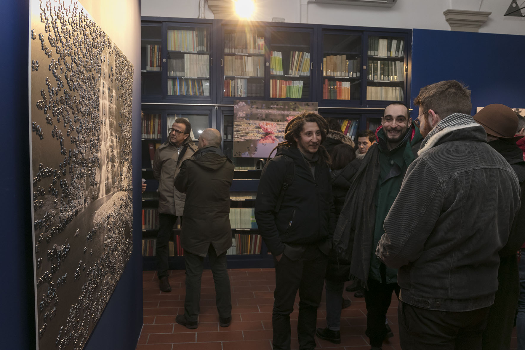 Un'immagine che ritrae giacca, cappotto, libreria, scaffalature e barba.