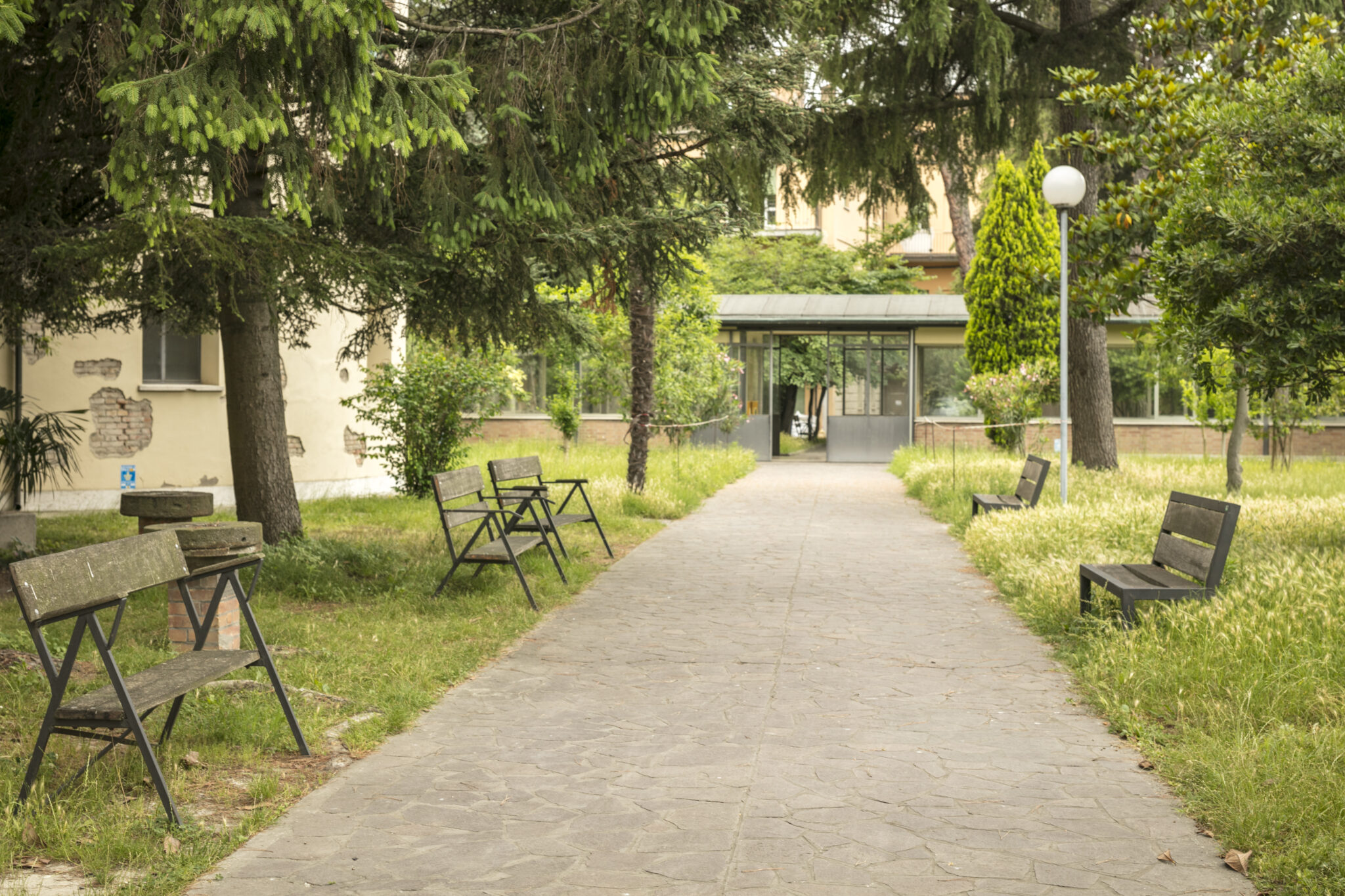 Un'immagine che ritrae spazio pubblico, arbusto, panchina da esterno, ombra e giardino.