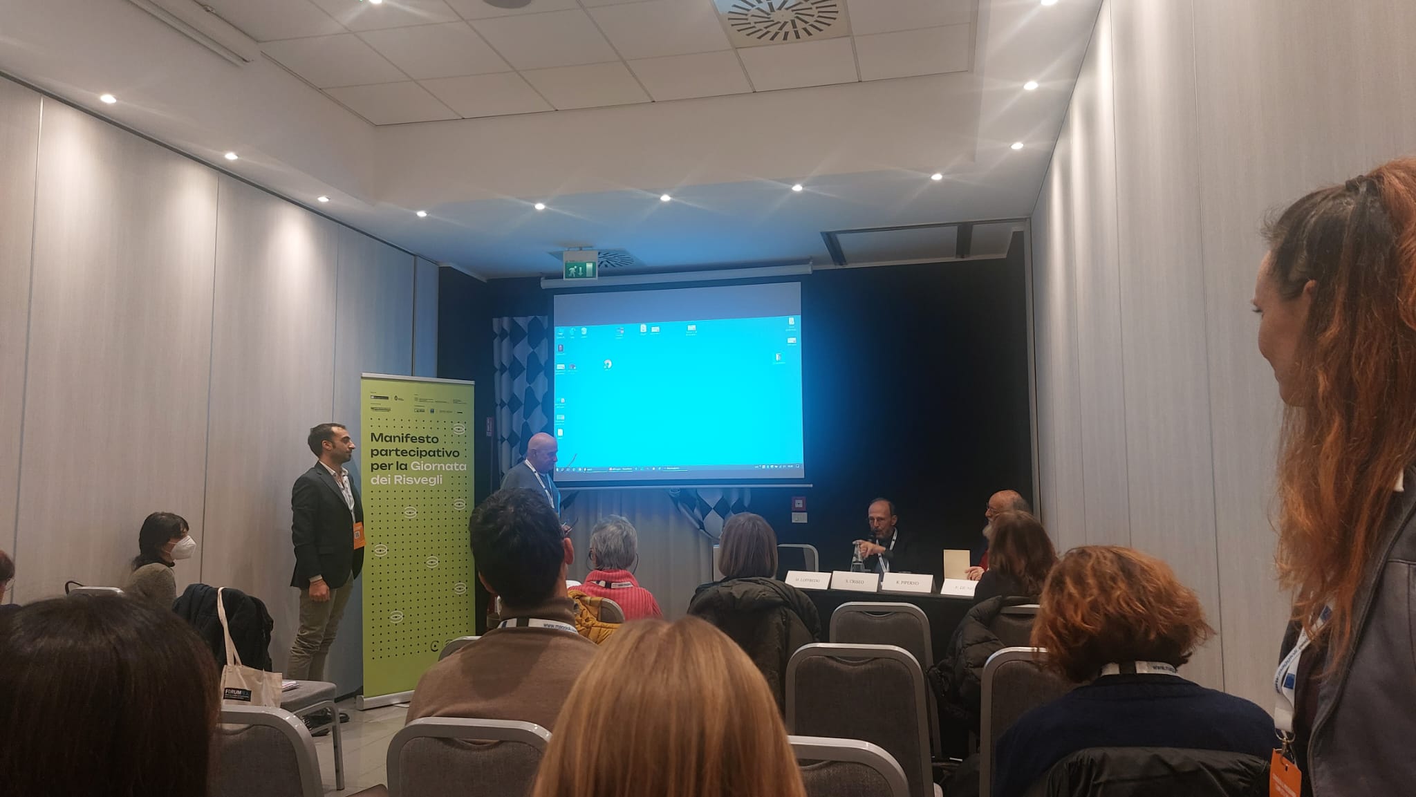 Un'immagine che ritrae dispositivo elettronico, presentazione, dispositivo di visualizzazione, evento e mobilia.