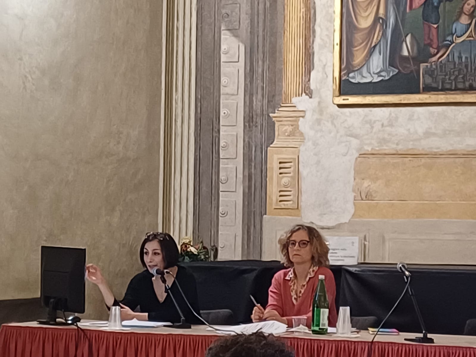 Un'immagine che ritrae mobilia, microfono, tavolo, dispositivo elettronico e cappotto.